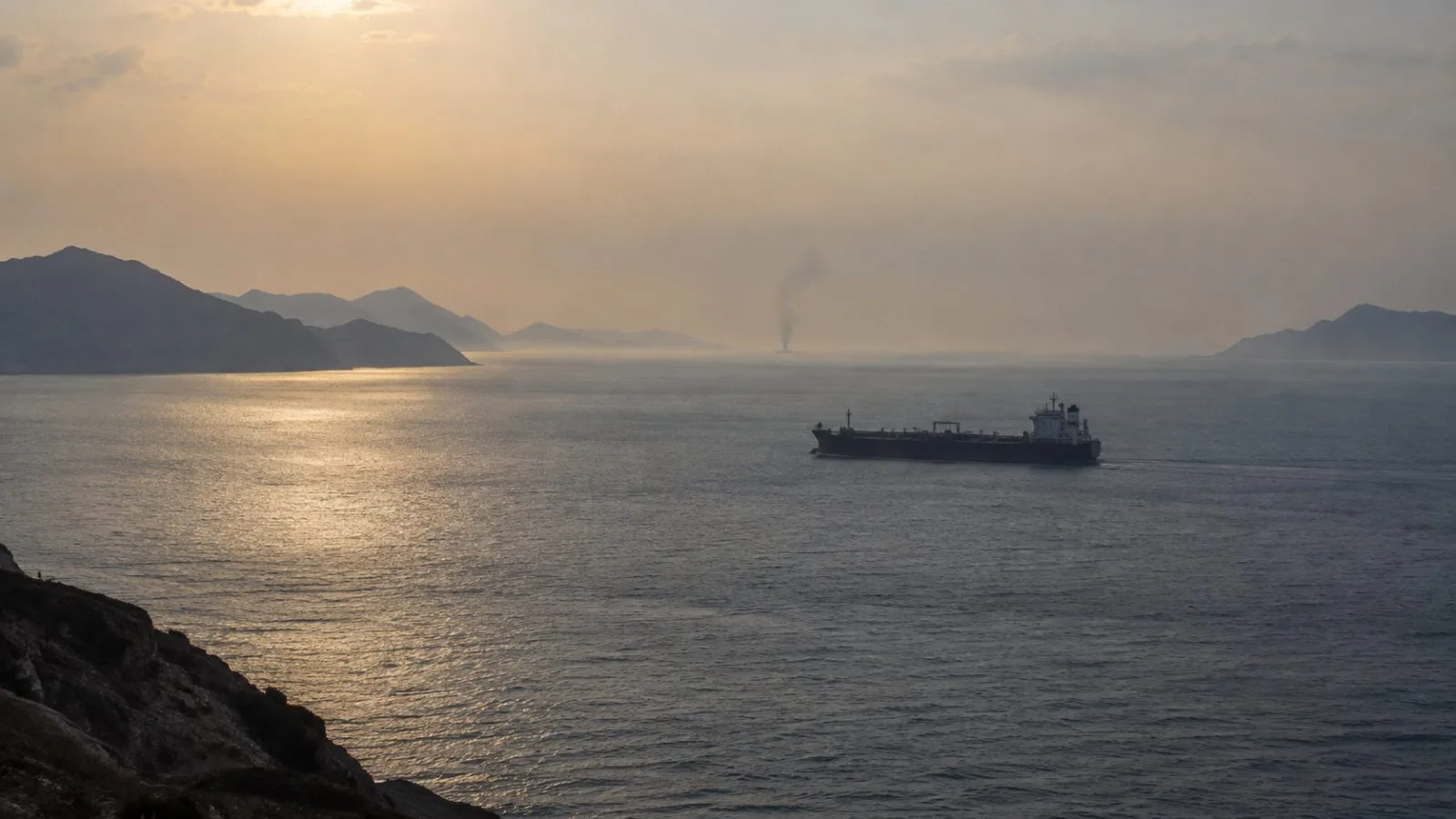 A tanker crosses hazy waters near a distant smoke plume / TokenPost.ai