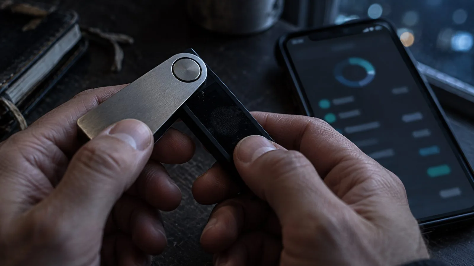 Hardware wallet and phone resting beside a dim window / TokenPost.ai
